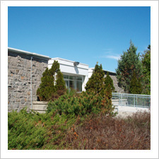 Exterior view of the former Gloucester Township Hall, built in 1962. The building is made of stone, and surrounded by green shrubs.